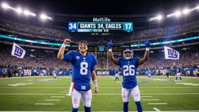A high-energy, cinematic view of a night football game at MetLife Stadium. A rookie New York Giants quarterback, number 8, stands in the end zone with his right fist raised in triumph, smiling confidently. Beside him, a rookie Giants running back, number 26, is celebrating with both arms in the air. The bright scoreboard above them clearly shows 'GIANTS 34, EAGLES 17' in the 4th quarter. The stadium is packed with a roaring crowd waving blue and white Giants flags, celebrating a massive upset victory. Confetti is raining down, and bright stadium lights illuminate the thrilling scene